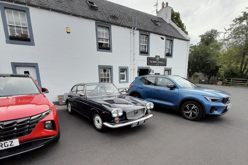 Lancia Flavia parked beside enormous modern SUVs